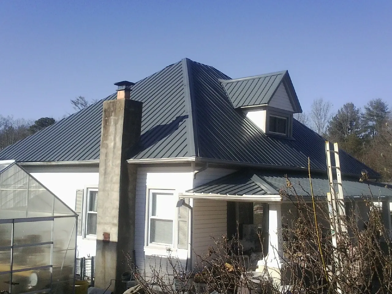 Dark blue standing seam metal roof on a white farmhouse with dormer — Slate & Tile Roof Repair by Roofing Brothers in La Prairie