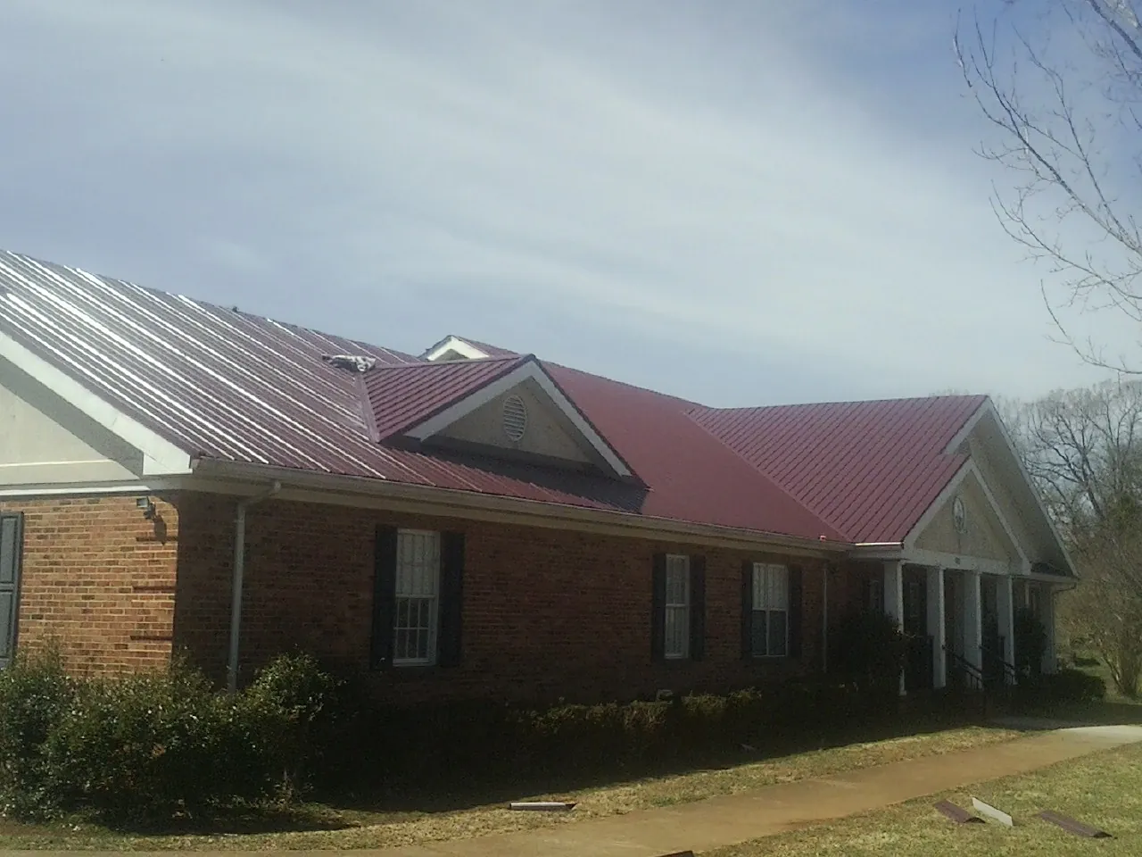 Red metal roof with gabled entries on a long brick building, from a Hail Damage Roof Repair job in La Prairie