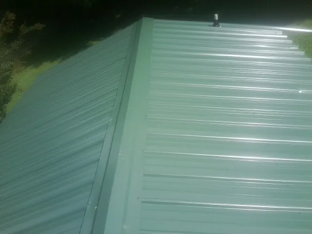 New green metal panels meeting at the ridge of a roof — Flat Roof Repair work by our crew in La Prairie