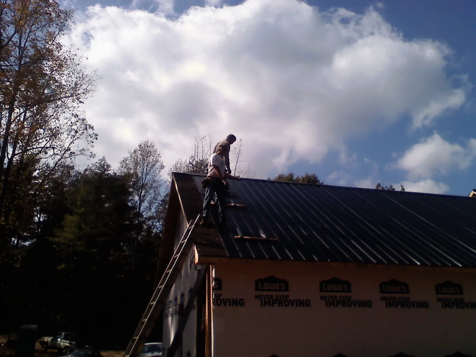 Roofer fastening dark metal panels high against a cloudy sky, from a Roof Inspection job in La Prairie