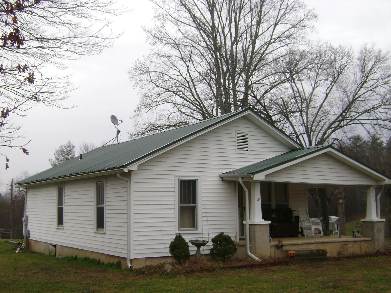 Green metal roof on a white bungalow with a side porch in La Prairie