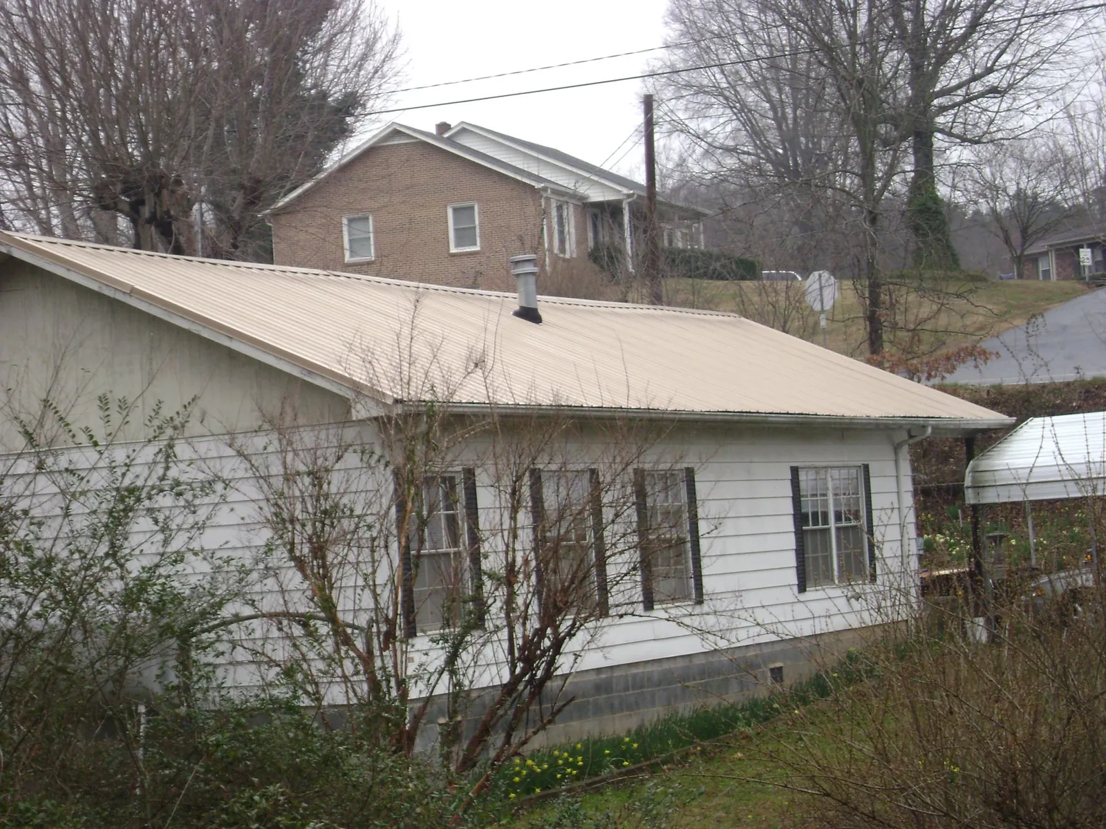 Tan metal roof on a white sided house set into a hillside — Commercial Roofing by Roofing Brothers in La Prairie